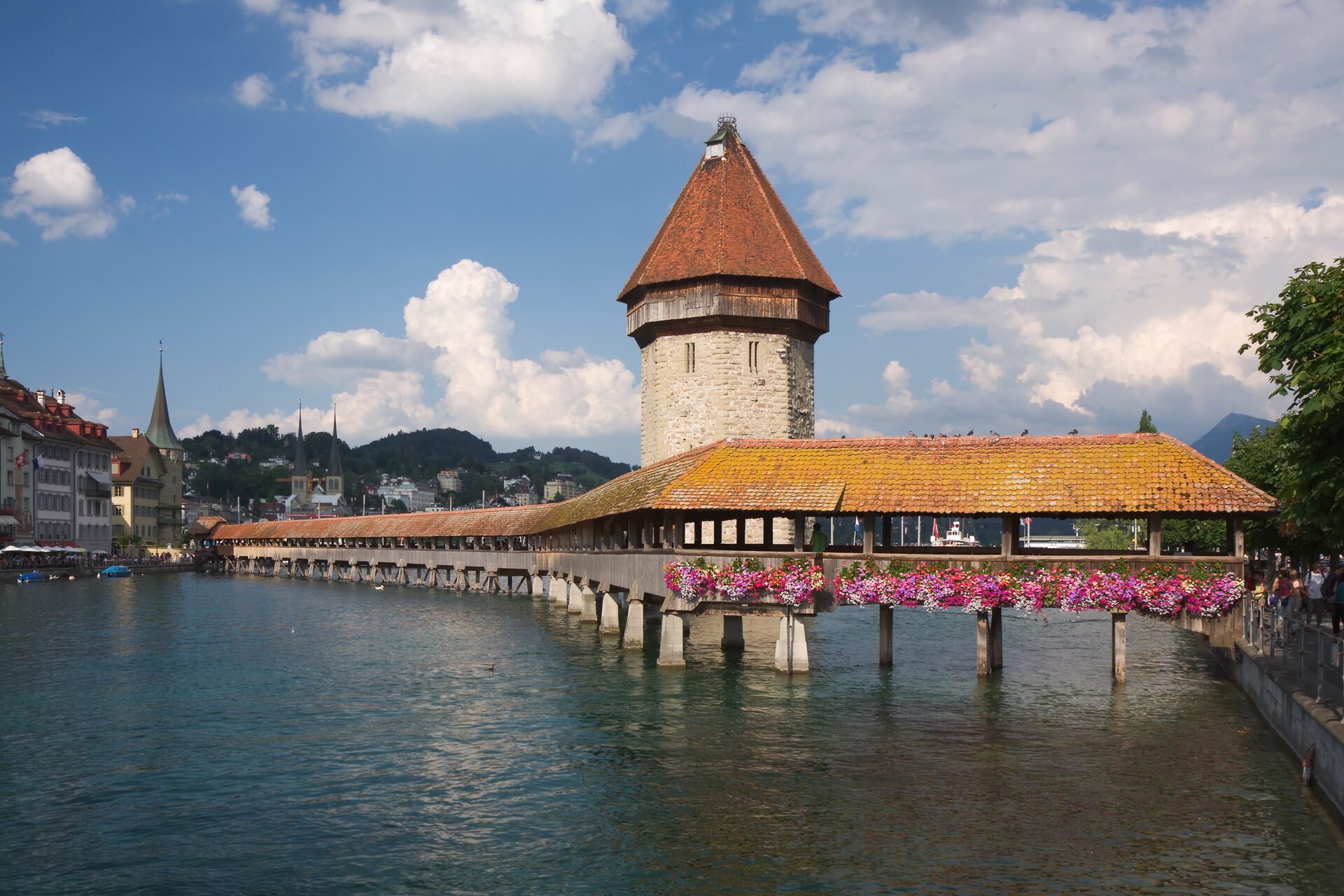 The wooden Chapel Bridge with its stone water tower over the Reuss in Lucerne, flower boxes on the bridge and the old town behind