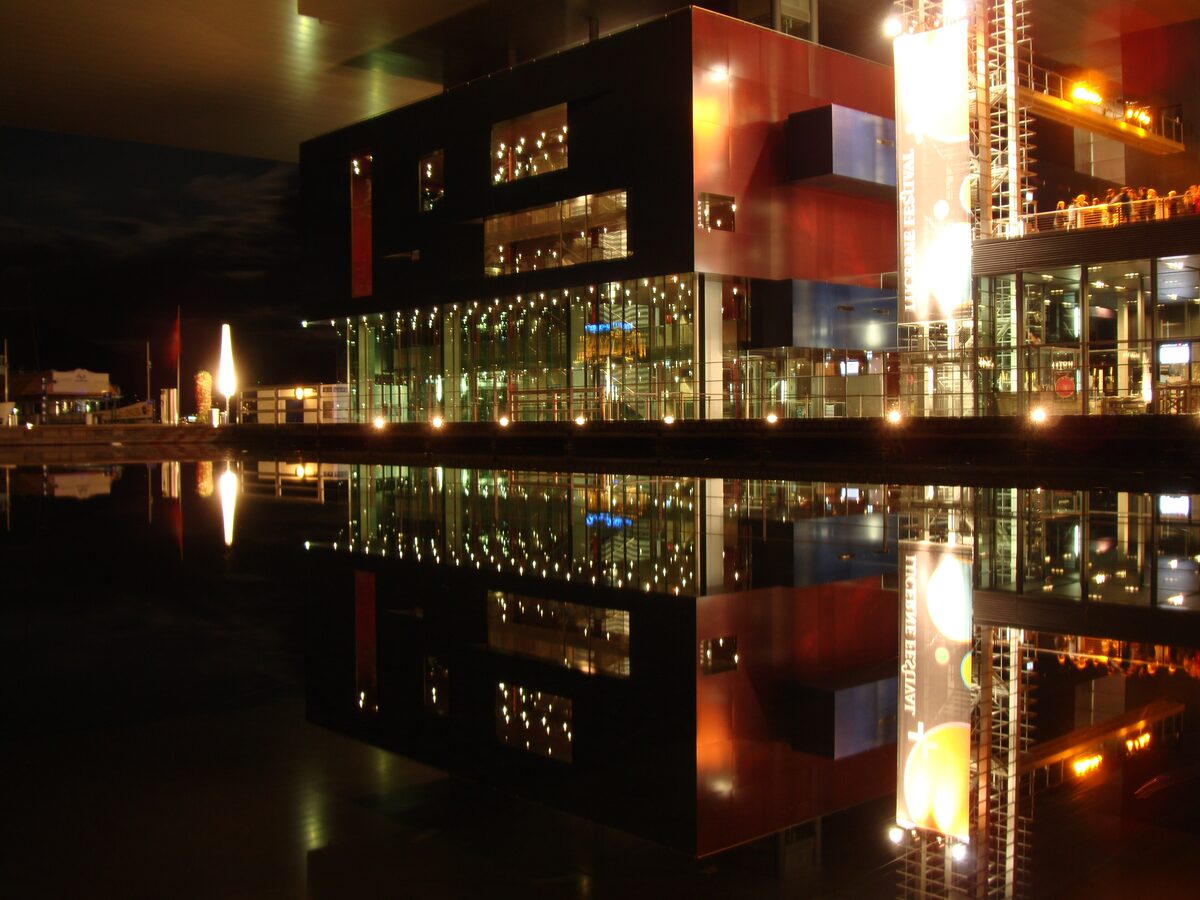 The KKL at night, its lit glass front and red-and-black volumes mirrored in the still water of the lake