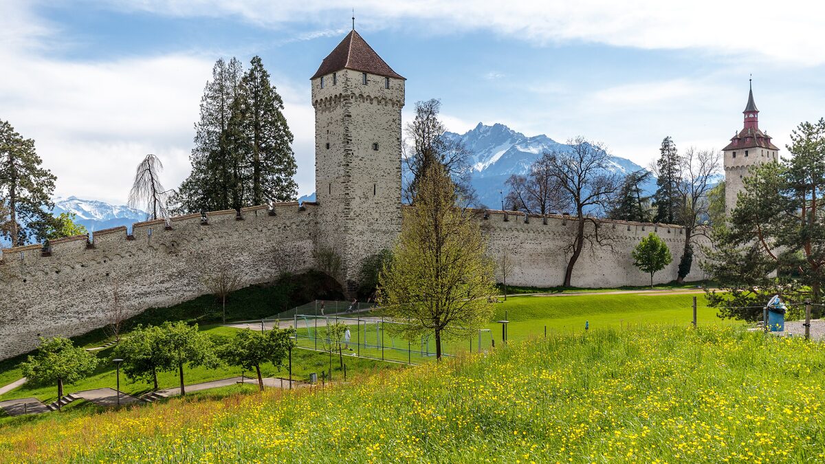 The Museggmauer wall with its round towers above a green meadow, snowy peaks behind