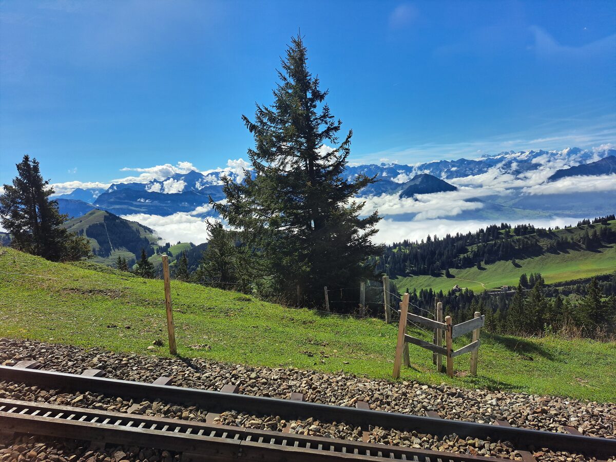Grass slopes and the rack railway track on the Rigi, with the Alps and a sea of cloud beyond