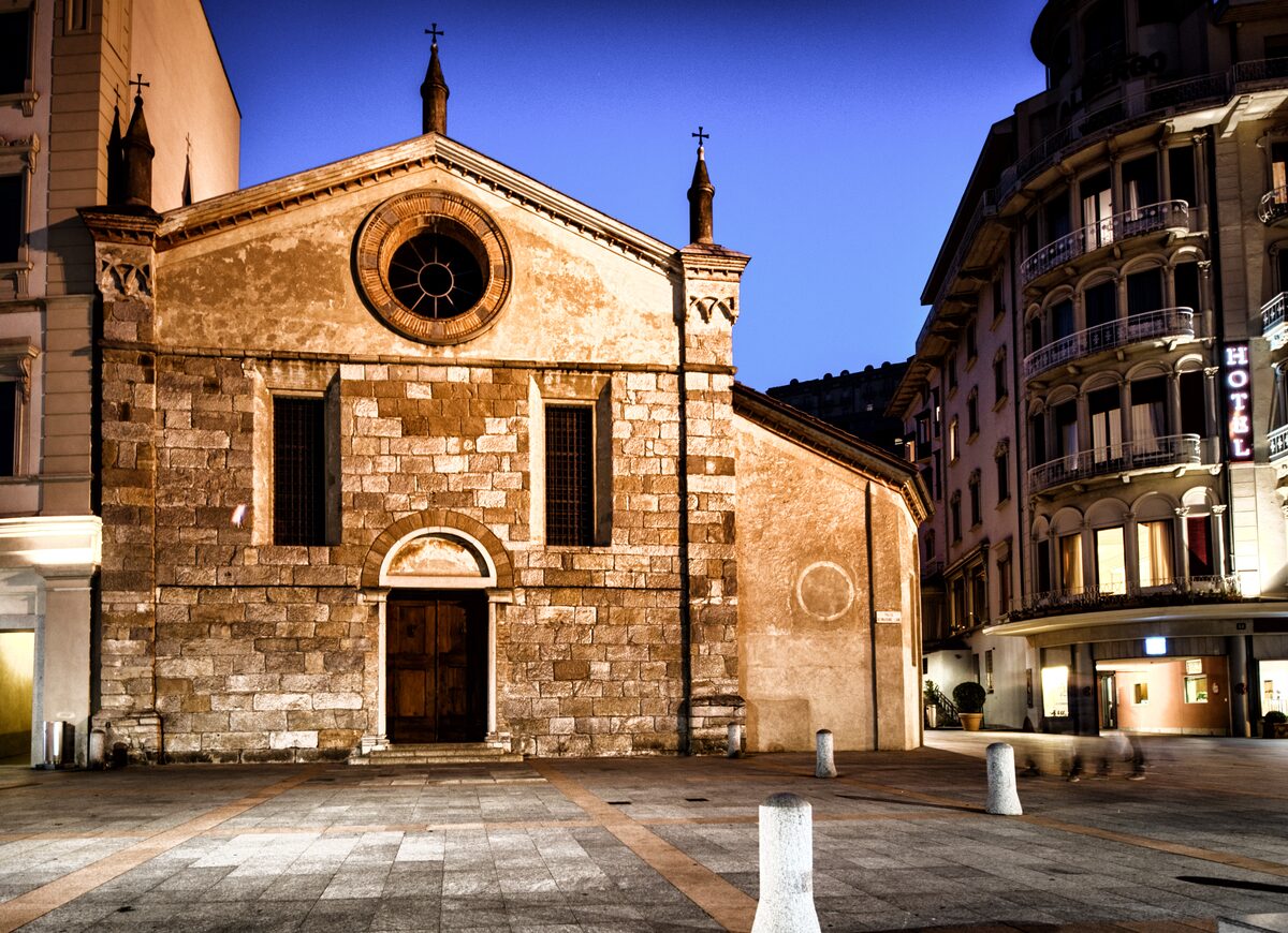 The stone facade of Santa Maria degli Angioli with its round window, between hotel buildings at dusk