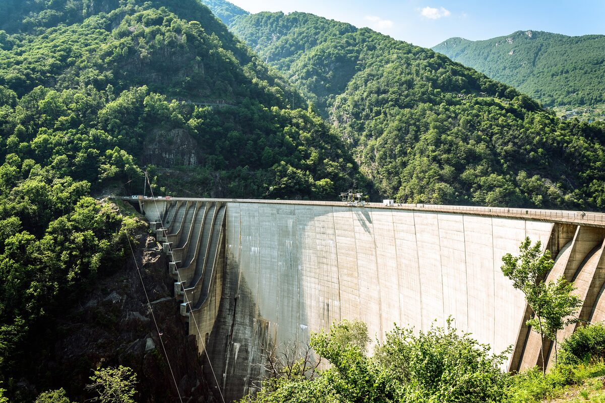 The curved concrete wall of the Contra Dam with wooded slopes of the Verzasca valley around it