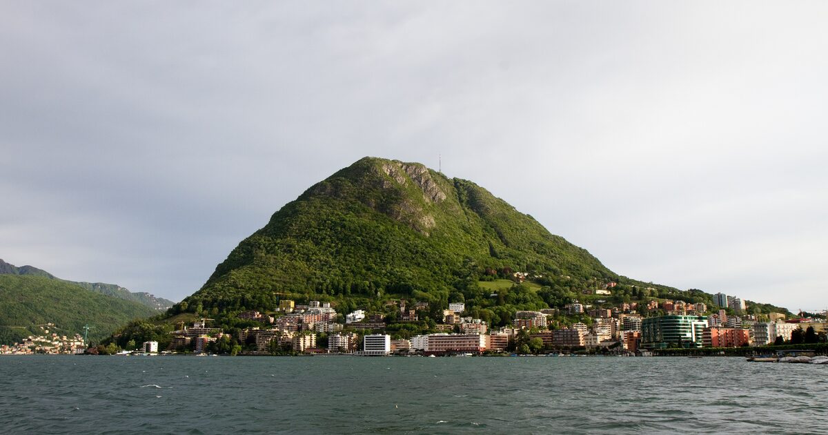 Monte San Salvatore rising above the lakeshore villages of Lake Lugano under a pale sky