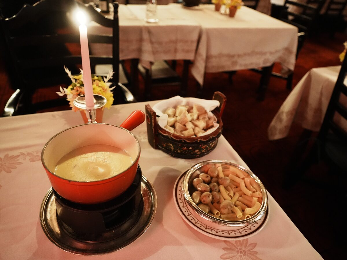 A pot of melted cheese fondue with bread cubes and side dishes on a restaurant table