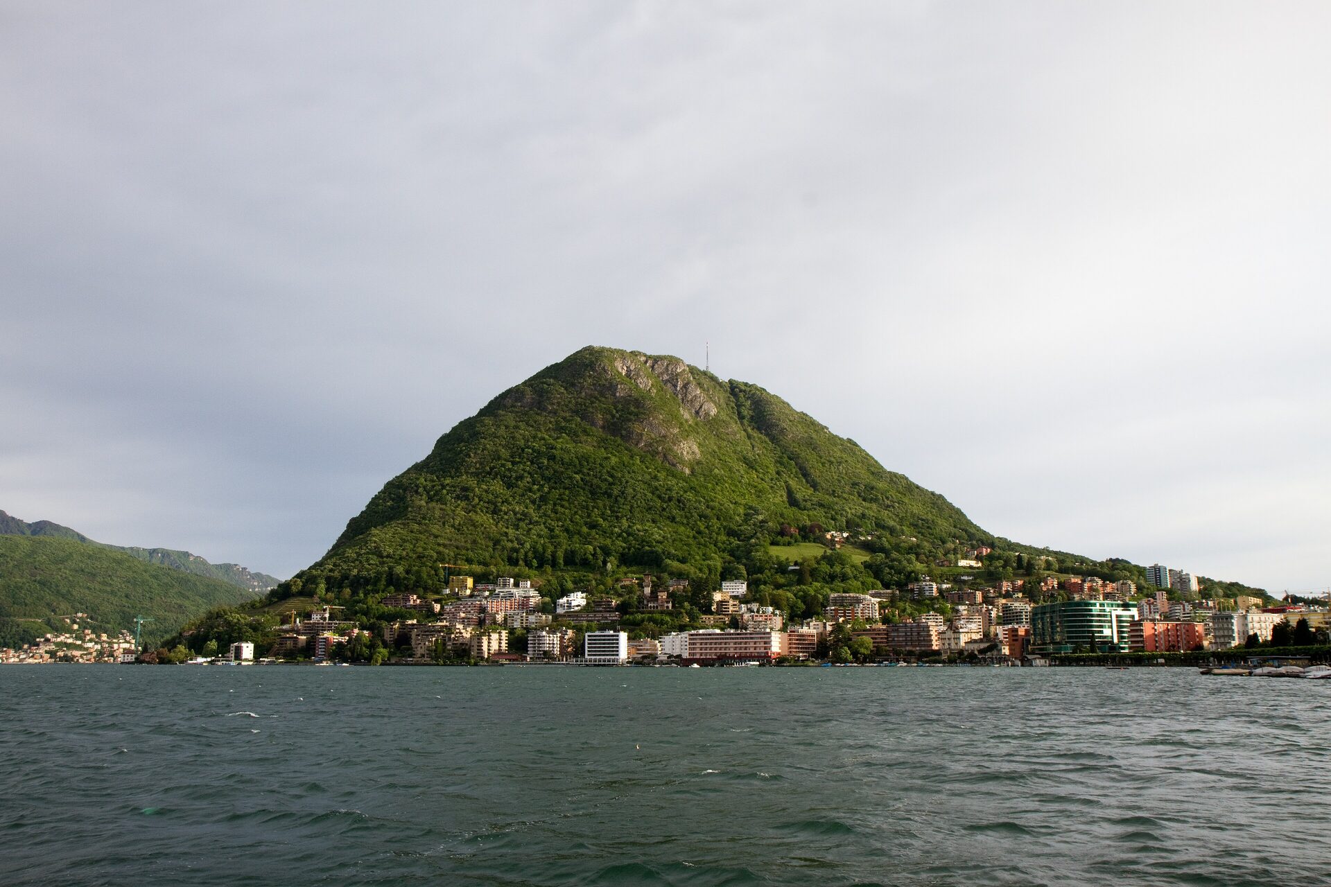 Monte San Salvatore rising above the lakeshore villages of Lake Lugano under a pale sky