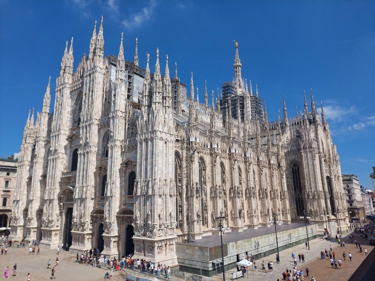 Milan Cathedral's white marble spires and gothic facade above the crowds on the piazza