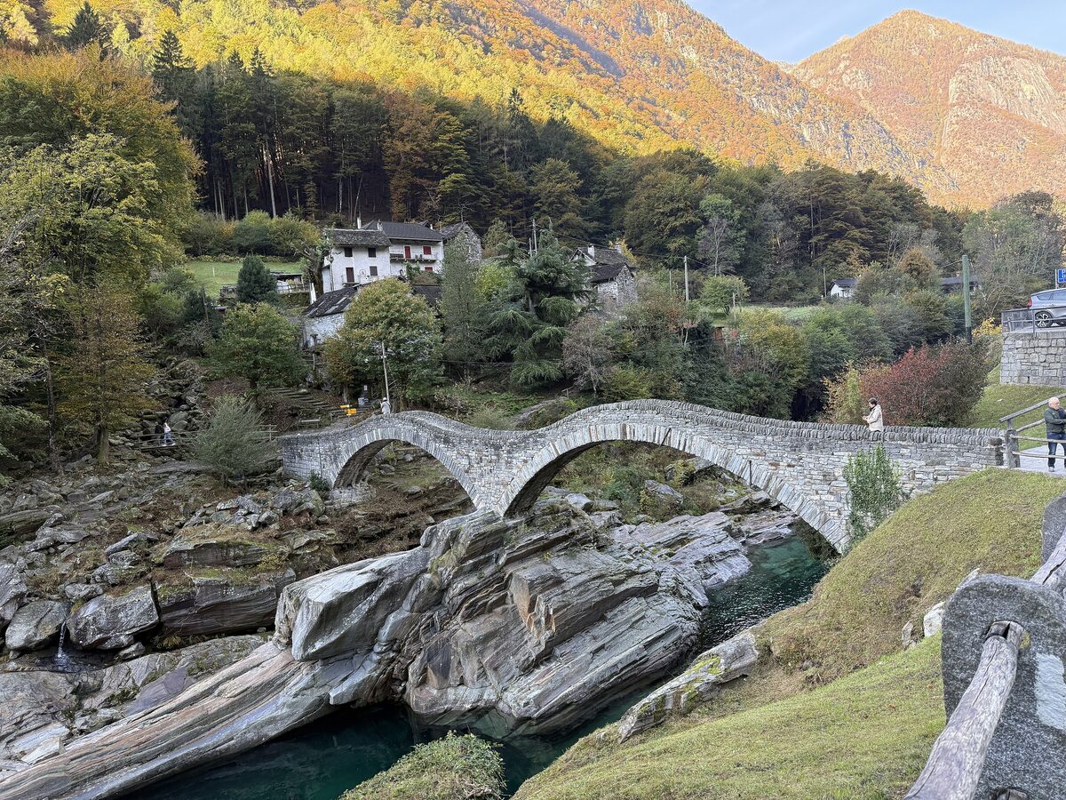 The two-arched stone Ponte dei Salti over the Verzasca river, with yellowing trees on the slopes