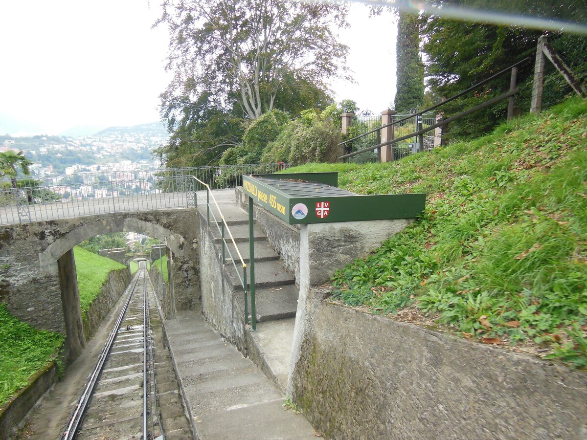 The rails and stone steps of the San Salvatore funicular climbing through the green hillside