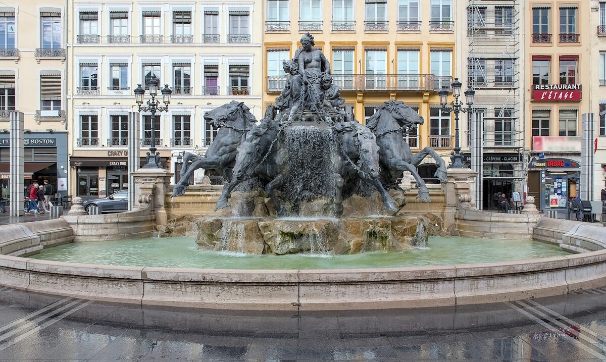 The Bartholdi fountain on the Place des Terreaux, a woman driving a chariot pulled by four rearing horses, with tall city buildings behind
