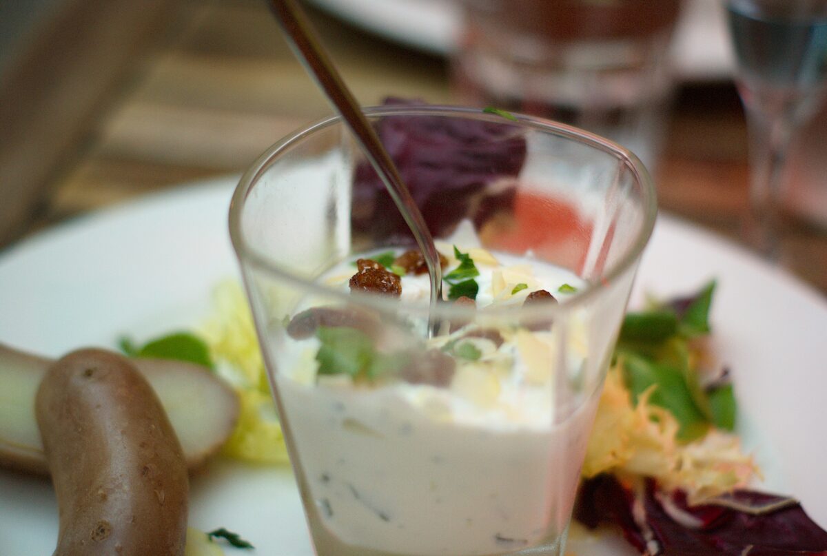 A glass of cervelle de canut, white herbed cheese, on a plate with a small sausage, beetroot and salad