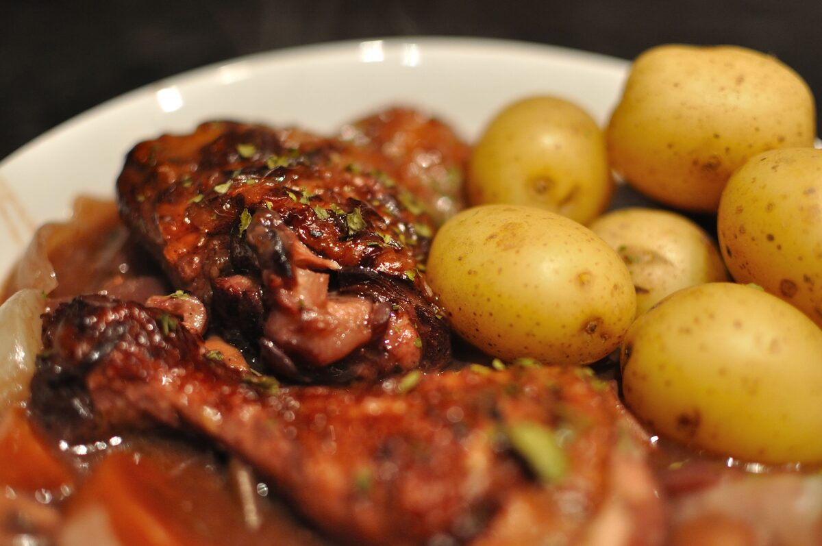 Pieces of chicken in a dark red wine sauce with boiled new potatoes on a plate