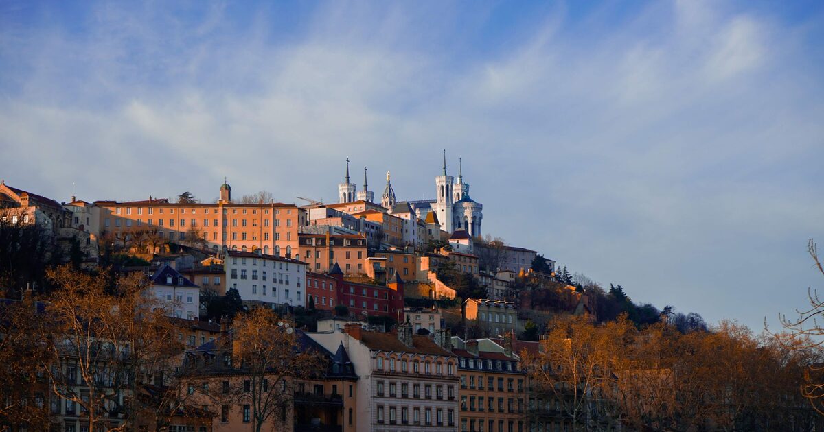 Fourvière hill in Lyon in warm evening light, with the white basilica on top above old ocher and pink houses and bare autumn trees