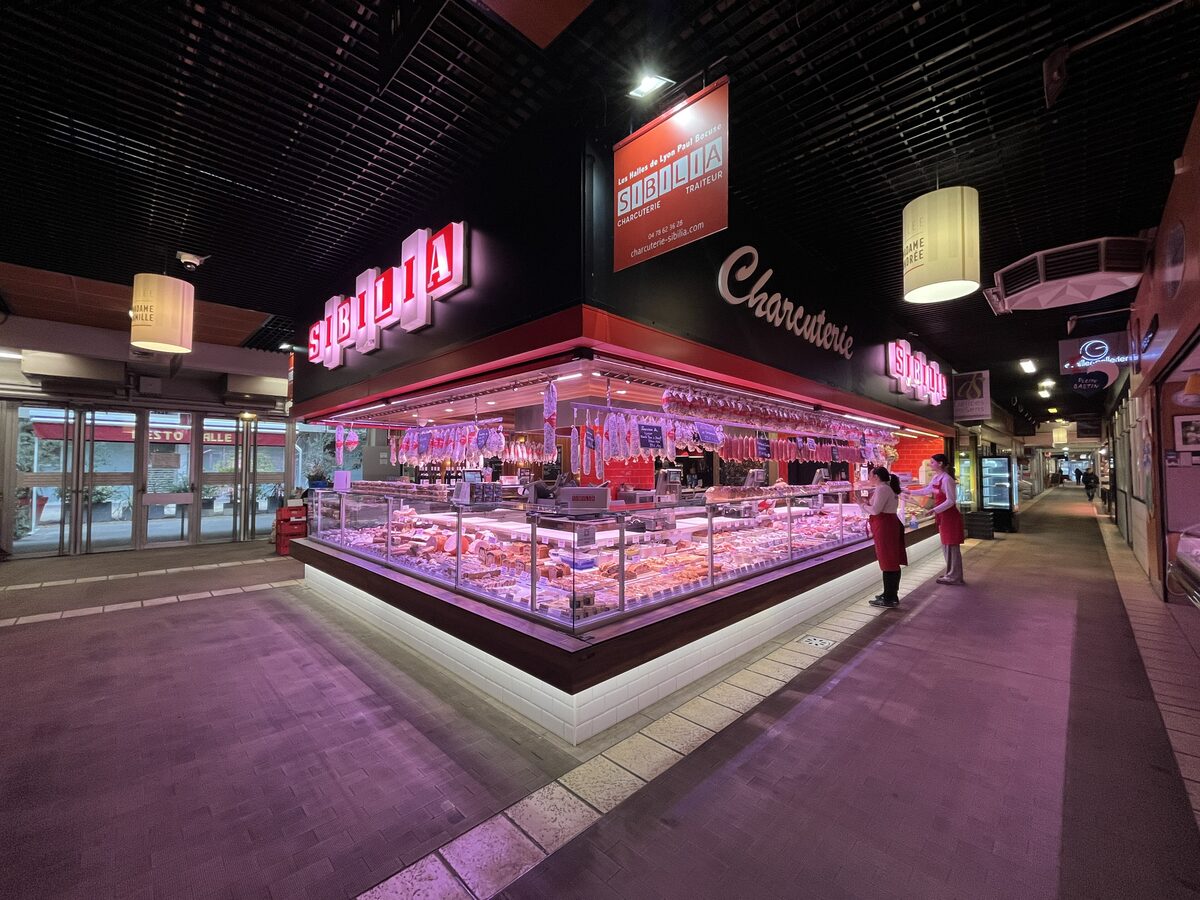 The brightly lit counter of the Sibilia charcuterie inside Les Halles de Lyon Paul Bocuse, with hams and sausages behind glass