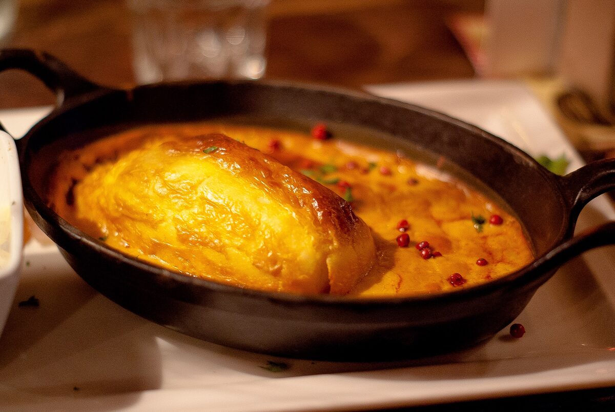 A golden, puffed pike quenelle in a creamy orange Nantua sauce in a small cast-iron dish