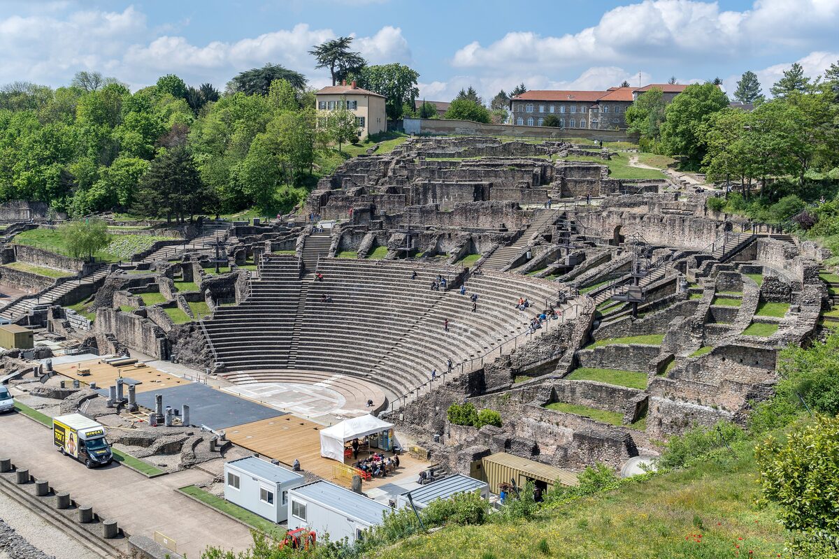 The stone tiers of the Roman theater of Fourvière curving around its stage, with trees and old buildings on the hill above