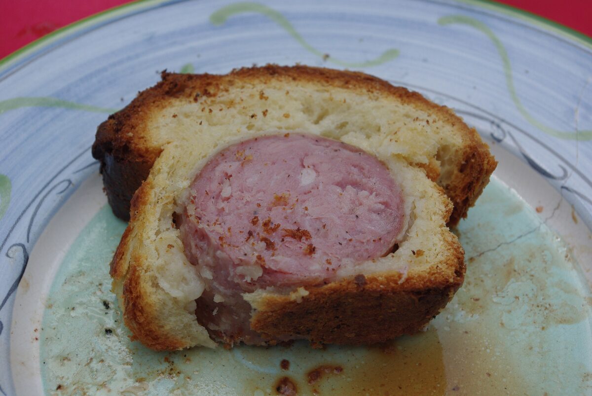 A thick slice of saucisson brioché, a pink sausage baked inside golden brioche, on a plate