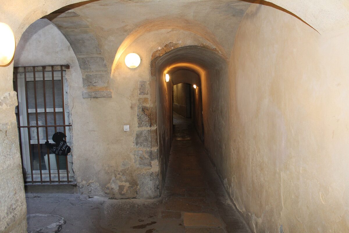 A narrow vaulted passage with stone walls and a lamp, leading through an old building in Vieux Lyon