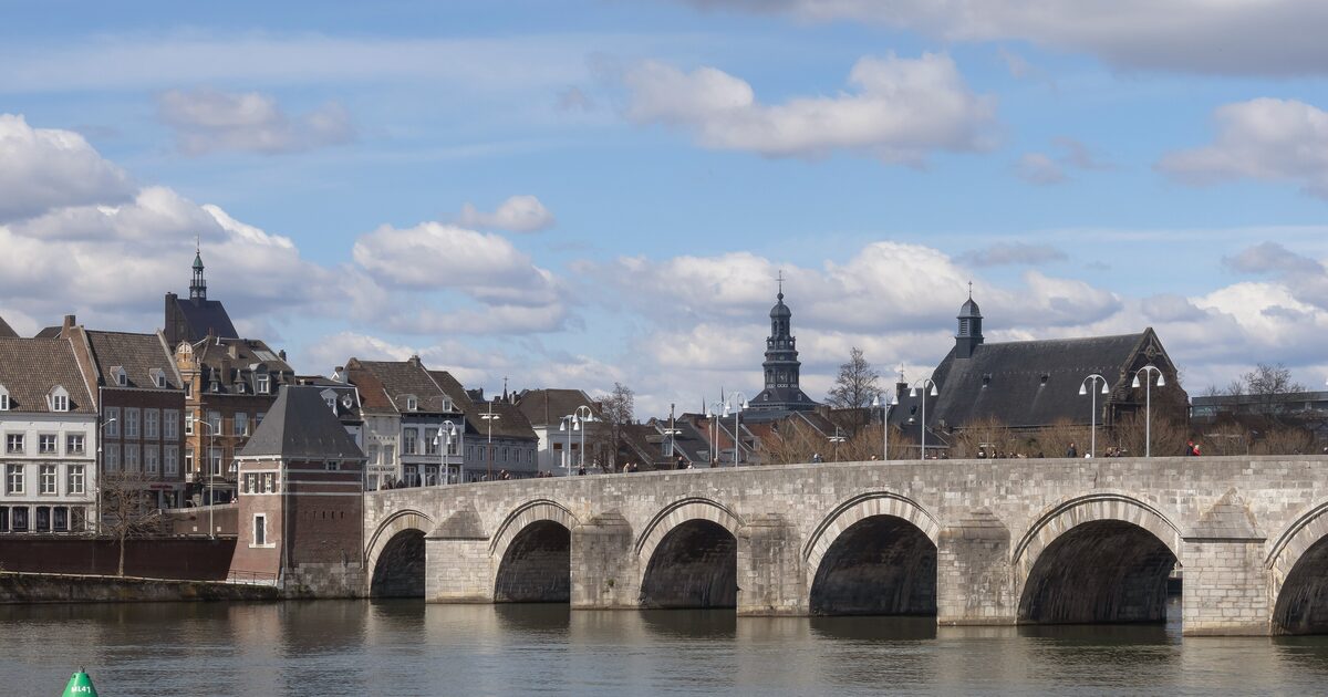 The stone arches of the Sint Servaasbrug over the Maas in Maastricht, with old houses and church towers behind under a blue sky with white clouds