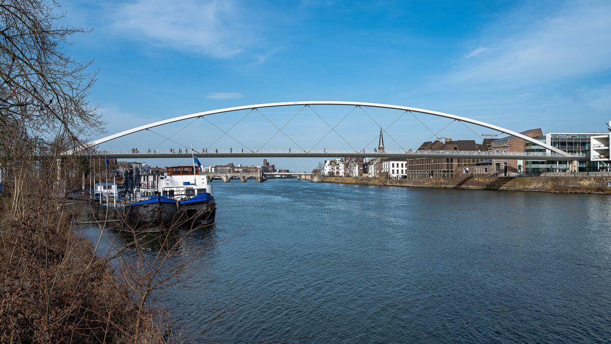 The white arch of the Hoge Brug footbridge over the wide Maas, with a barge moored on the left and the city beyond