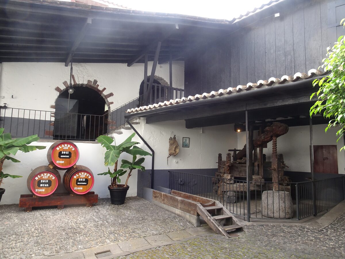 The cobbled courtyard of Blandy's Wine Lodge with small wine barrels, an old wooden wine press and whitewashed walls
