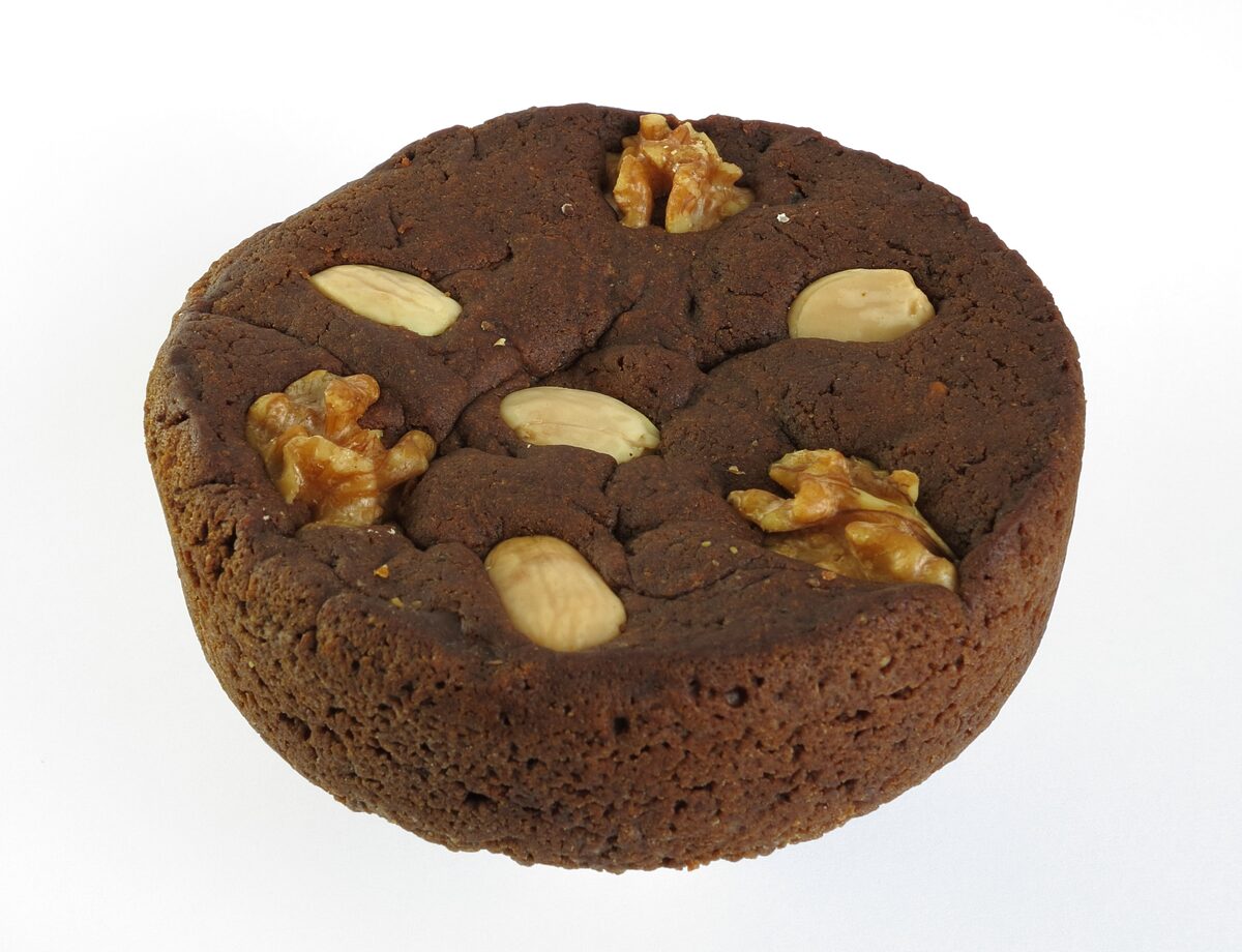 A round dark honey cake studded with almonds and walnuts on a white background