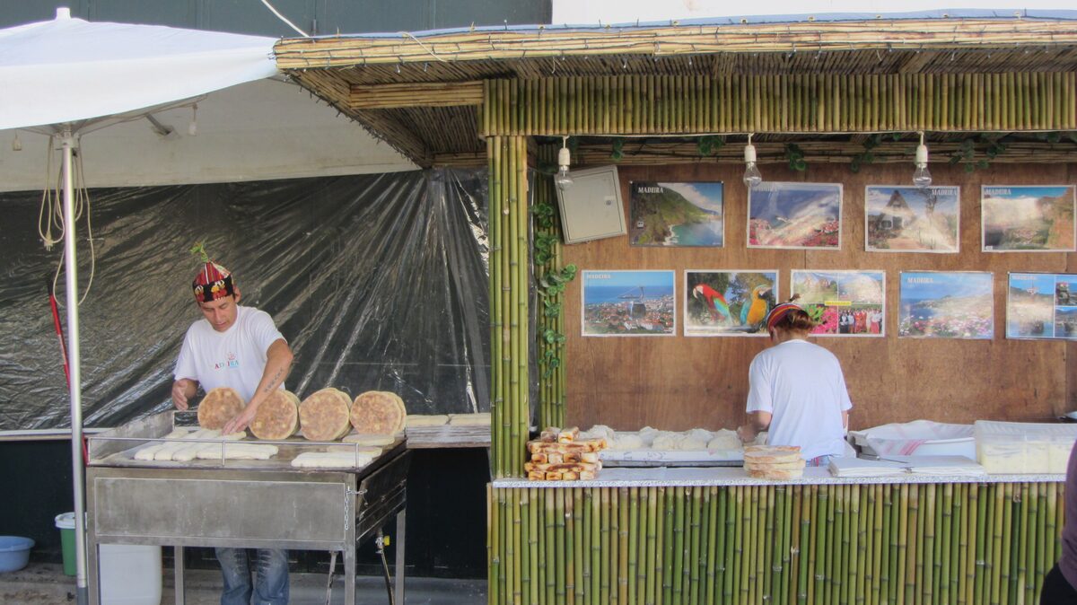 A market stall where a vendor cooks round flatbreads, with framed island pictures on the wall behind
