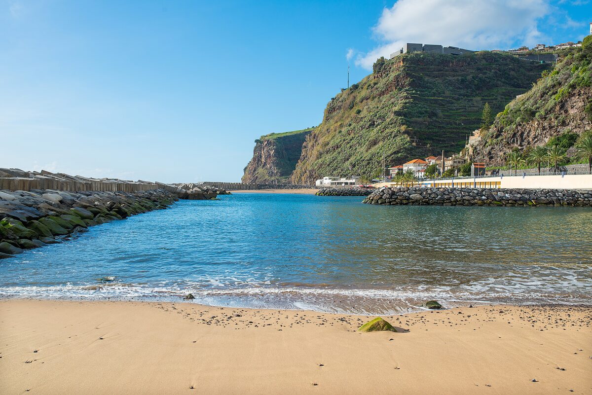 Golden sand and calm water at Calheta beach, with terraced cliffs and houses behind