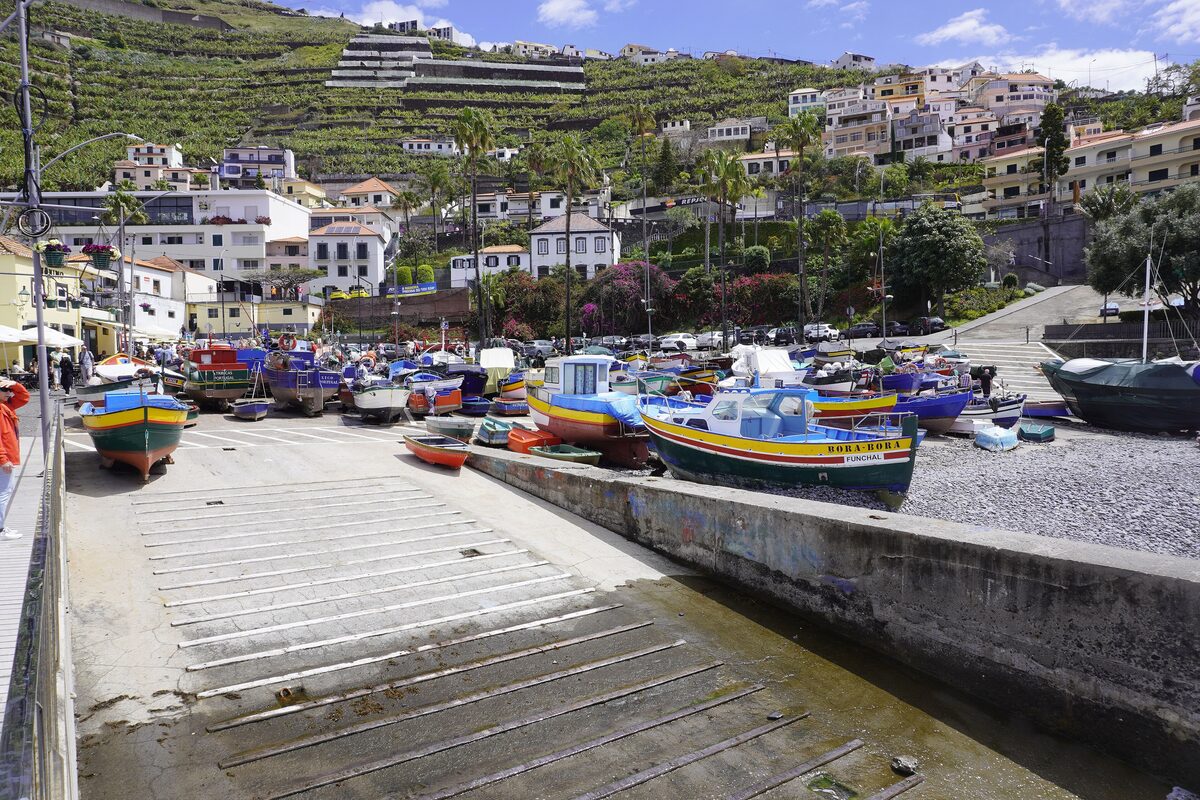 Brightly painted fishing boats pulled up on the slipway of Câmara de Lobos harbor, with terraced hills and white houses behind