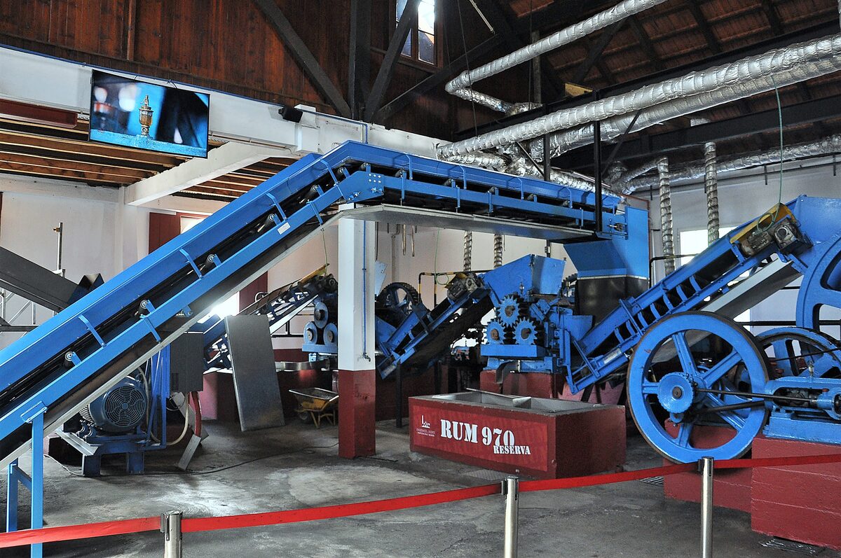 The old sugar cane mill at Engenhos do Norte, with blue conveyors and crushing machinery inside the distillery hall