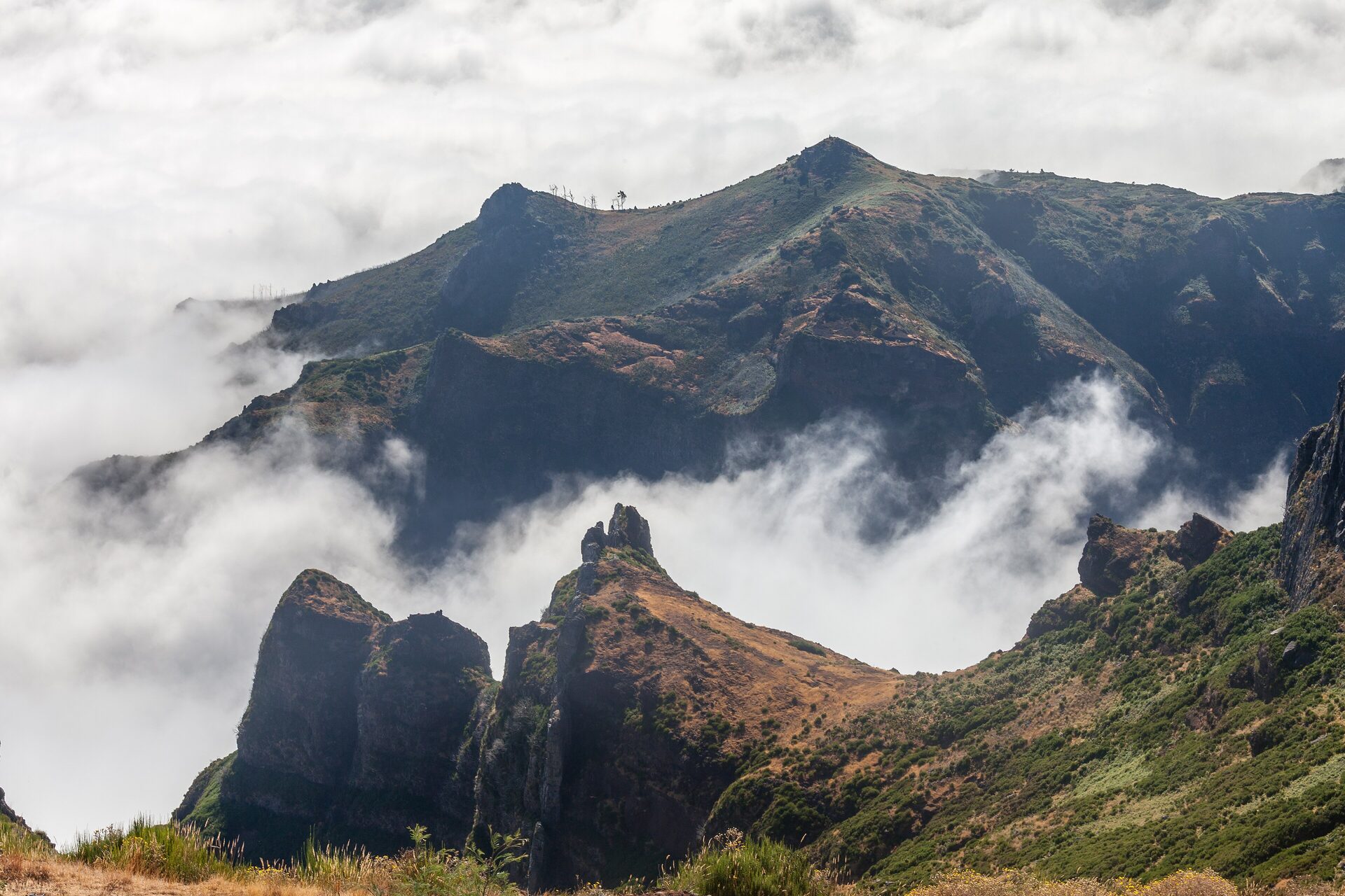 Rocky peaks of the central massif seen from Pico do Arieiro, rising out of a sea of cloud in bright daylight