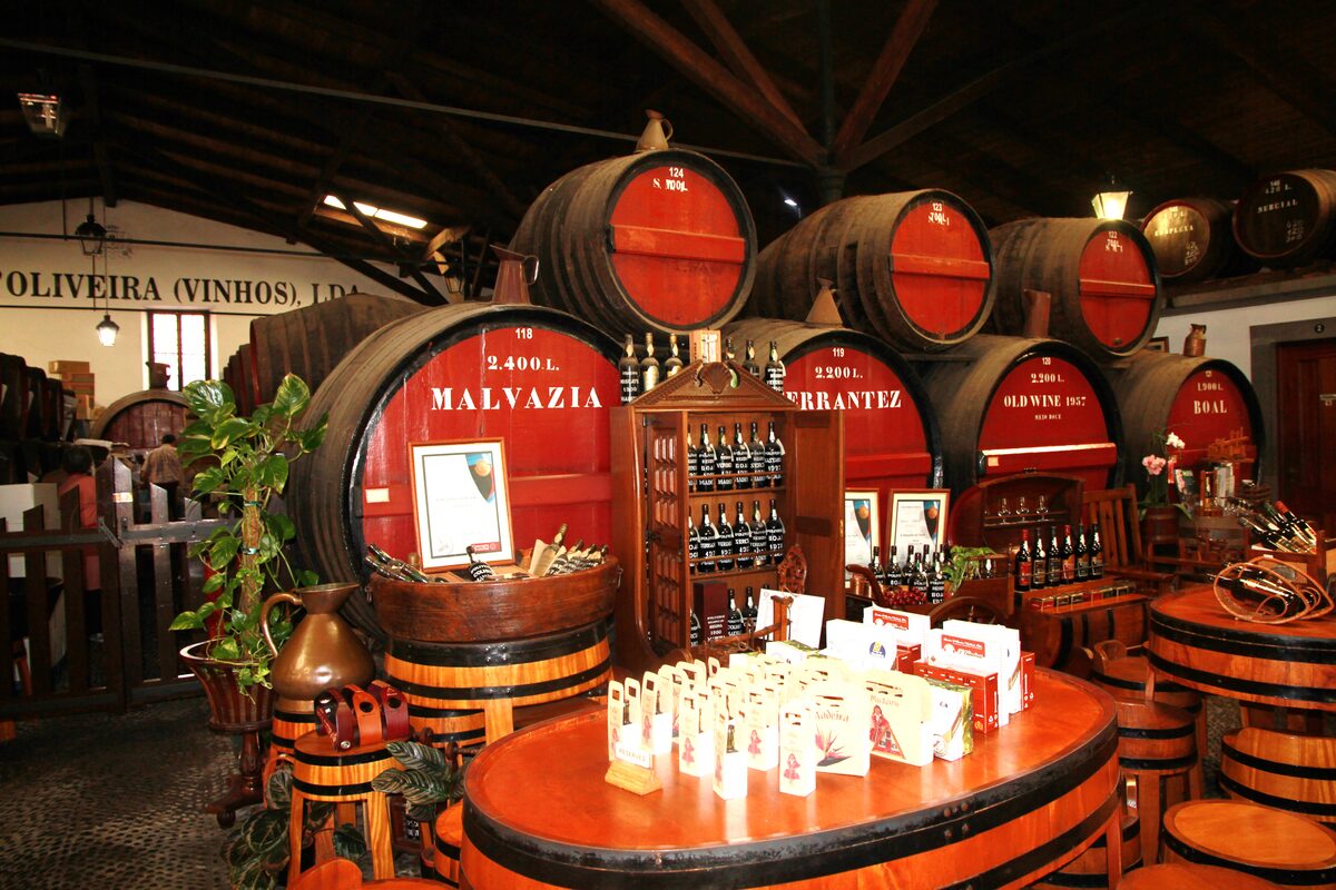 Big red-ended casks labeled Malvazia, Old Wine and Boal behind a barrel-top tasting table in a Funchal wine house