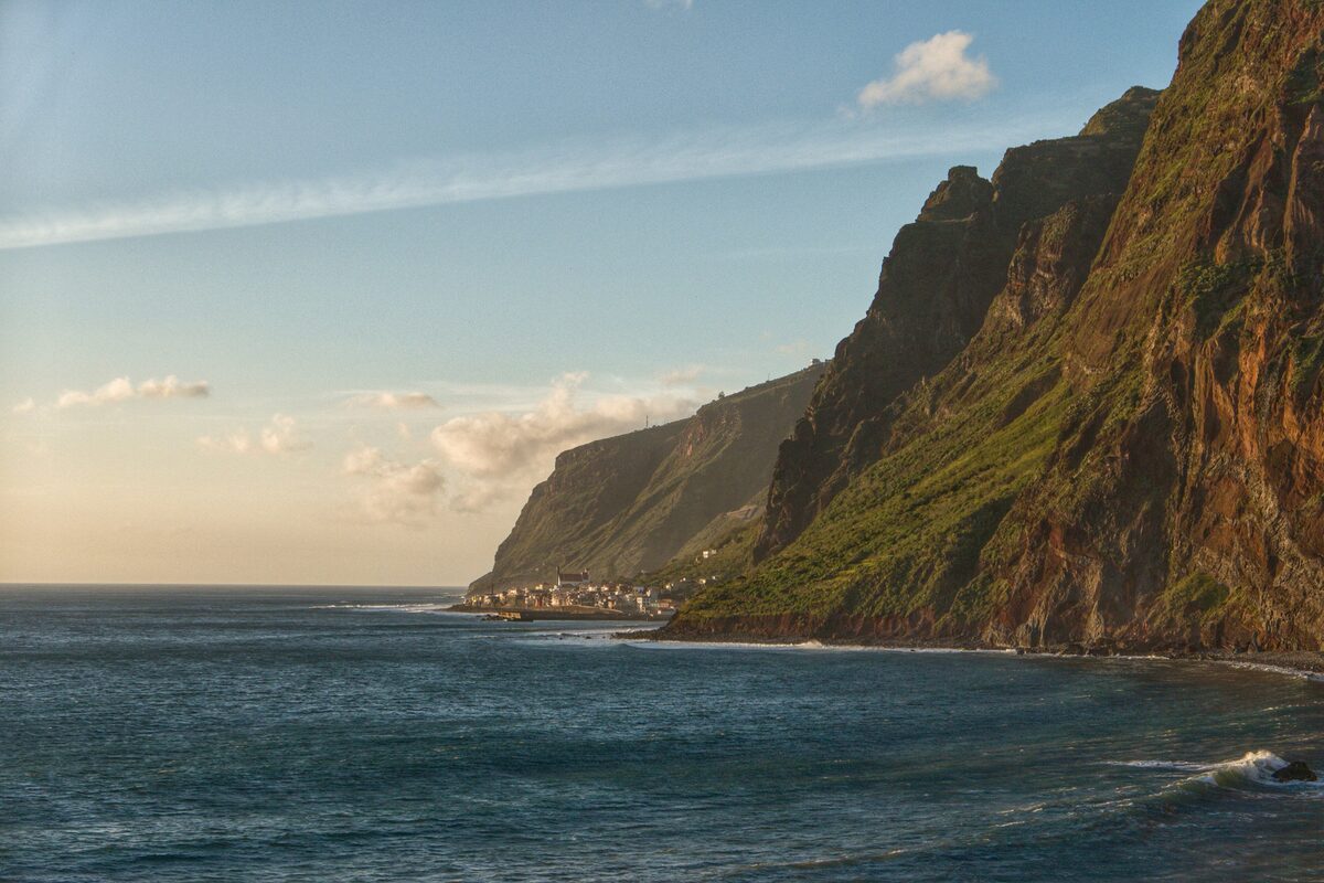 Steep green sea cliffs above the Atlantic, with a village at their foot near Paul do Mar