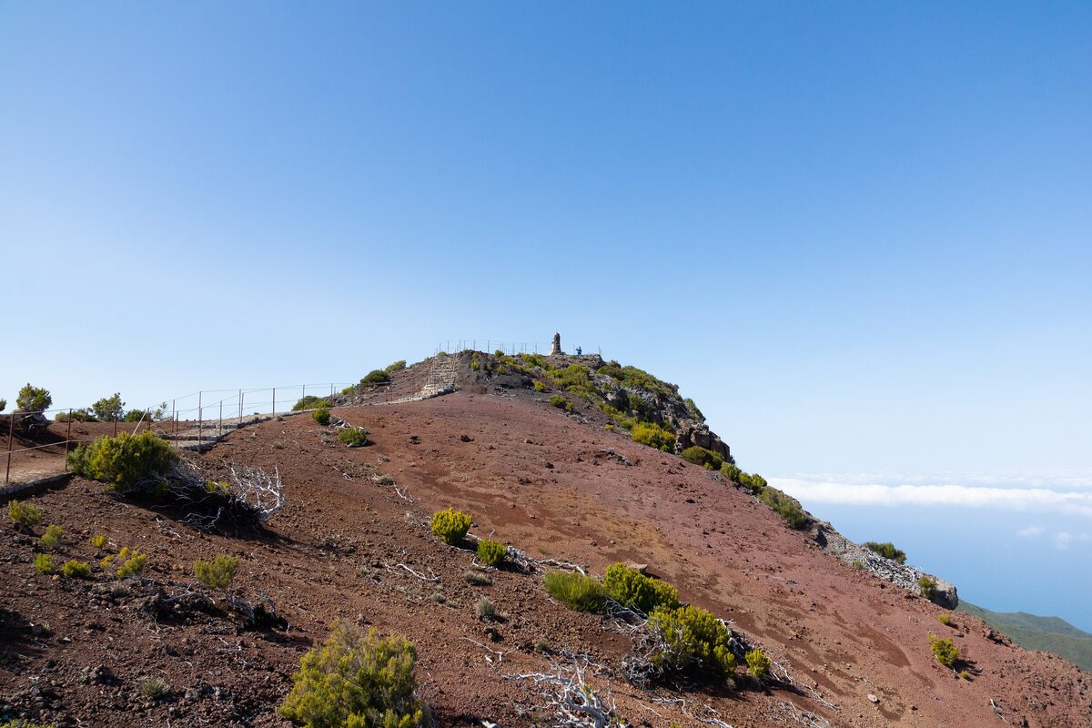 The bare red summit ridge of Pico Ruivo under a clear blue sky, with one small figure on the top