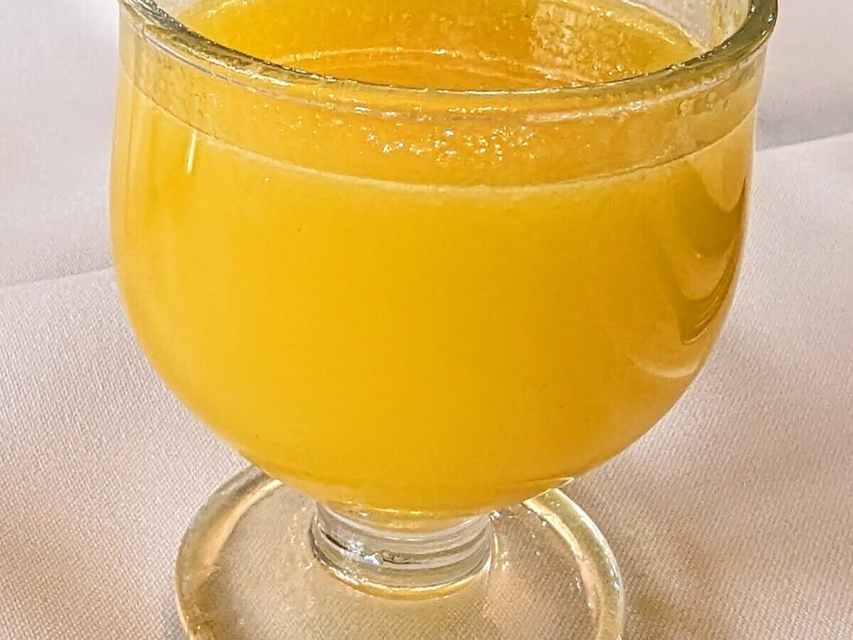 A stemmed glass of freshly poured, bright yellow poncha on a white tablecloth