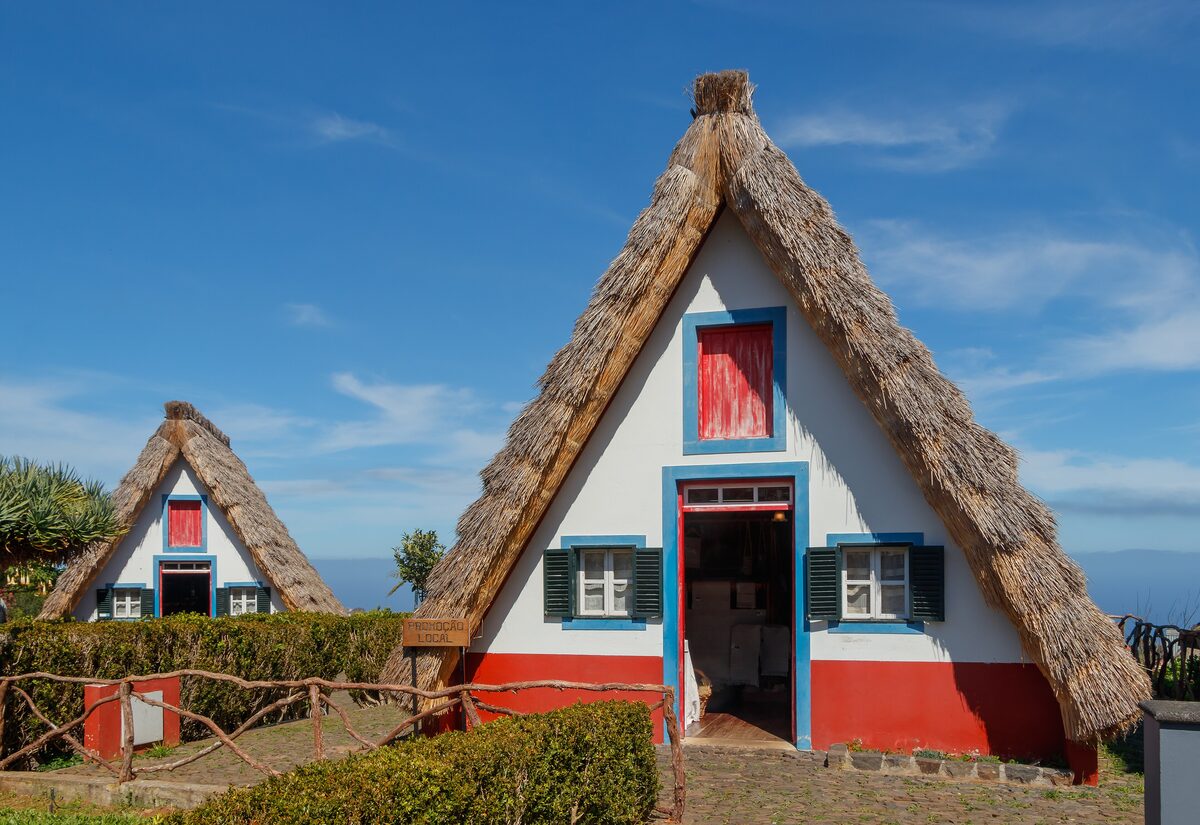 Two thatched A-frame cottages with red doors and blue trim in Santana