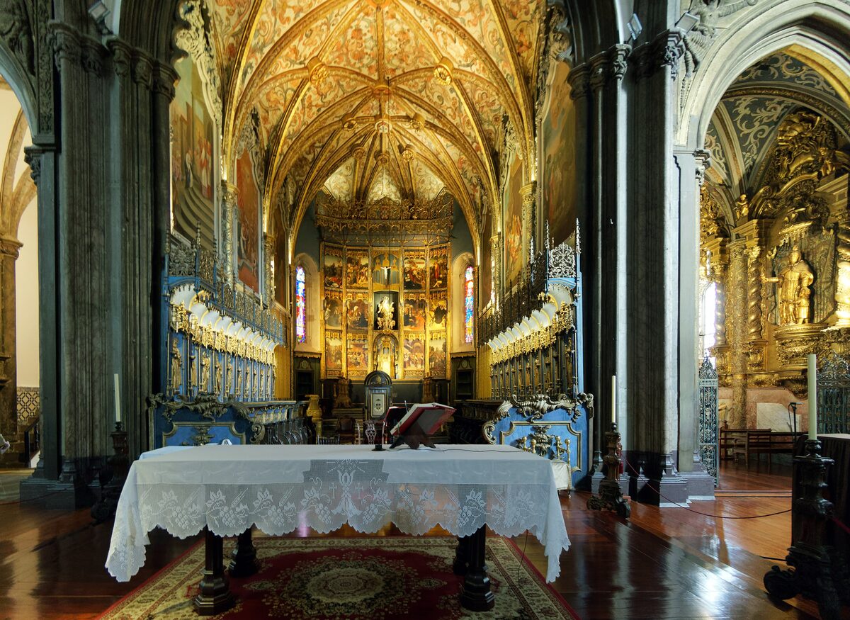 The gilded, painted vault over the high altar of Funchal cathedral, with carved choir stalls on both sides and a lace-covered altar table in front