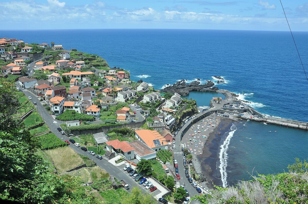 A black sand beach and harbor at Seixal, with village houses climbing the green slopes above