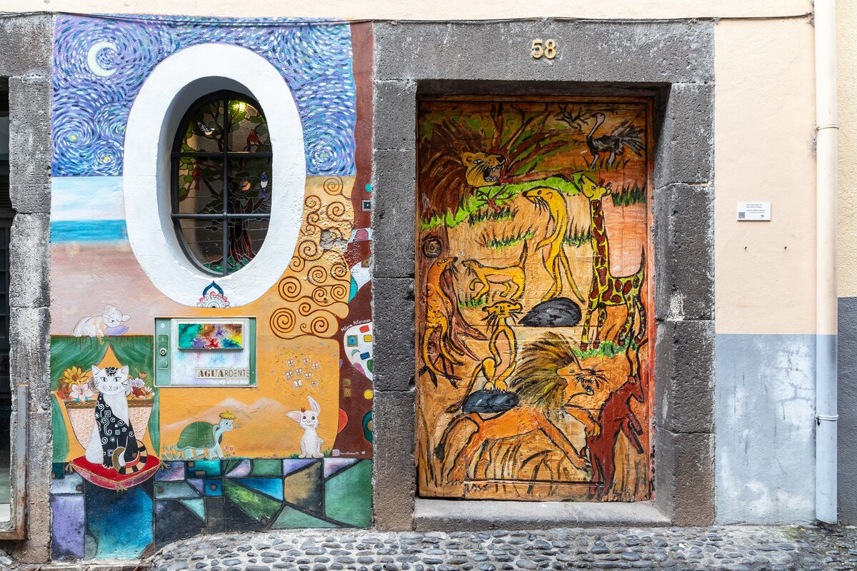 Two painted doors on Rua de Santa Maria, one with a giraffe and animal scene, beside a mural wall with a round window