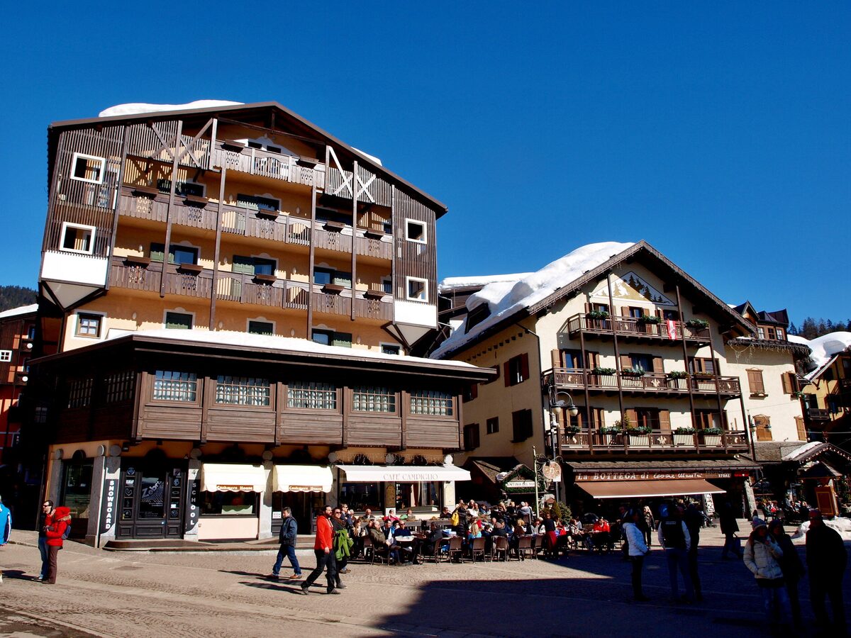 Chalet-style hotels and a busy café terrace on the main square of Madonna di Campiglio, with snow on the roofs