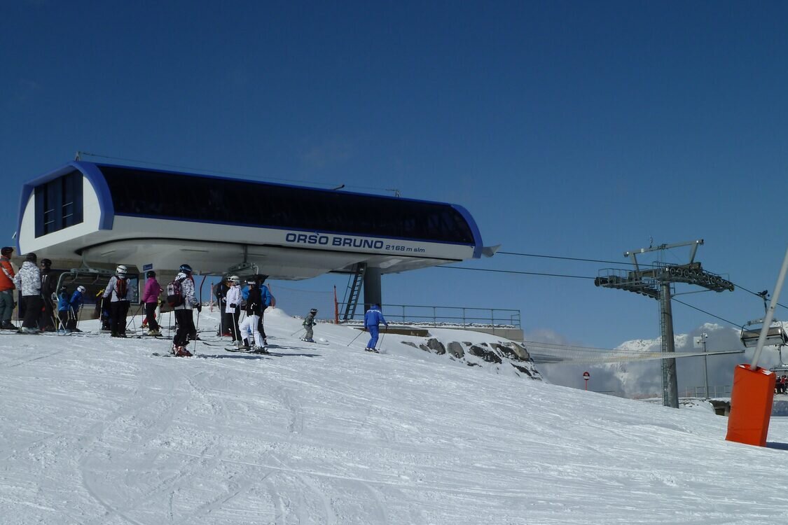 Skiers waiting at the top station of the Orso Bruno chairlift in Marilleva, on a sunny snowy slope under a blue sky