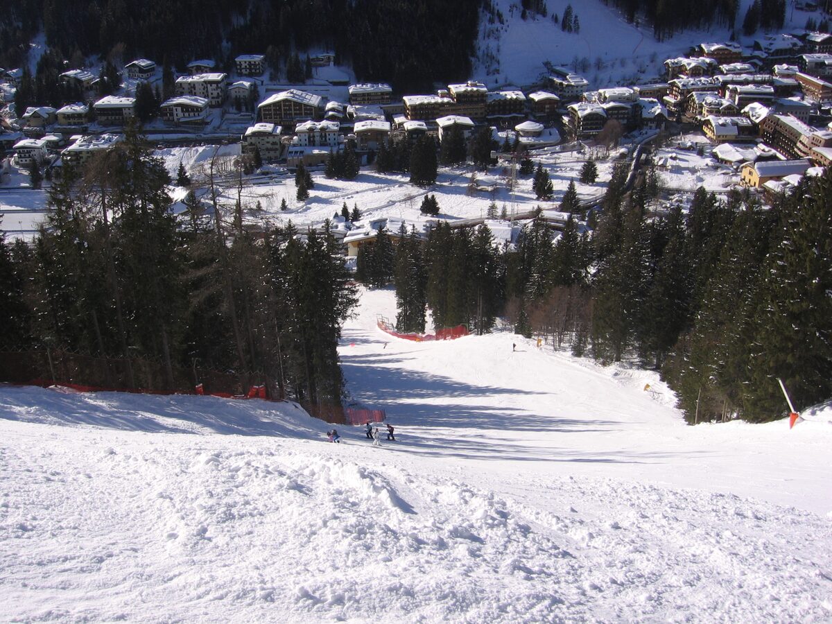 A red-netted ski slope running down toward the snow-covered rooftops of Madonna di Campiglio