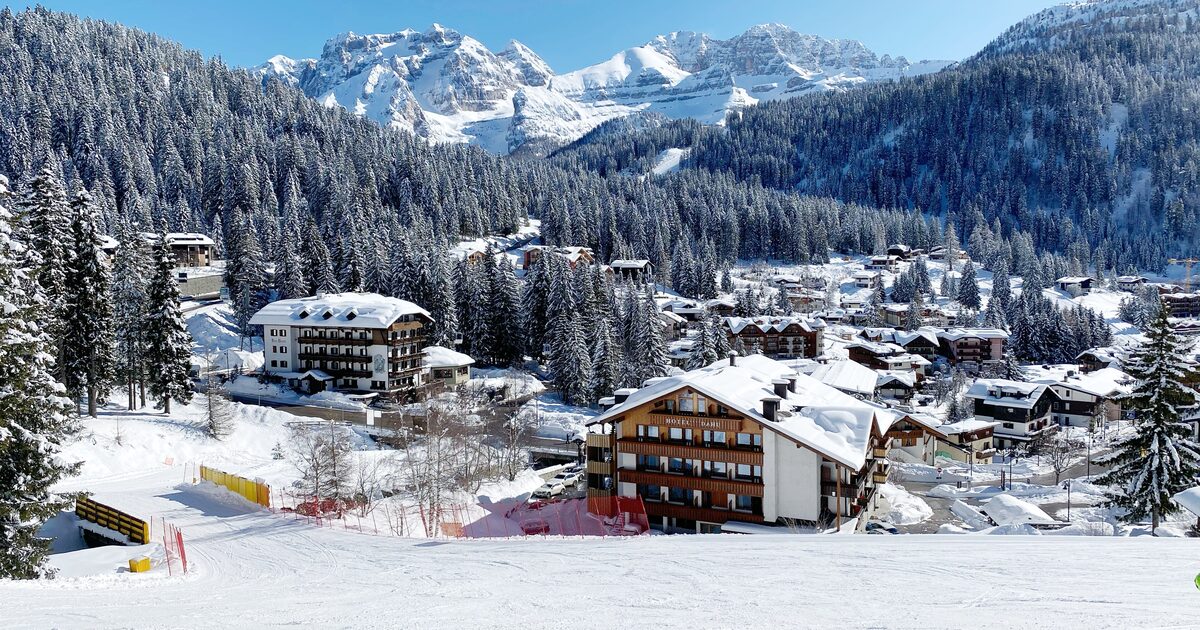Madonna di Campiglio under fresh snow on a bright winter day, with hotels and a piste in front of the Brenta Dolomites