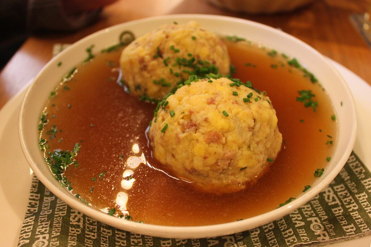 Two speck dumplings in a clear broth, topped with chopped chives