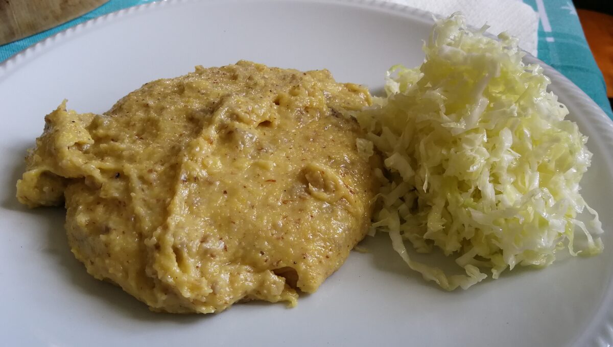 Soft polenta carbonera on a white plate beside a pile of shredded cabbage, a typical dish of Storo in the Giudicarie valleys