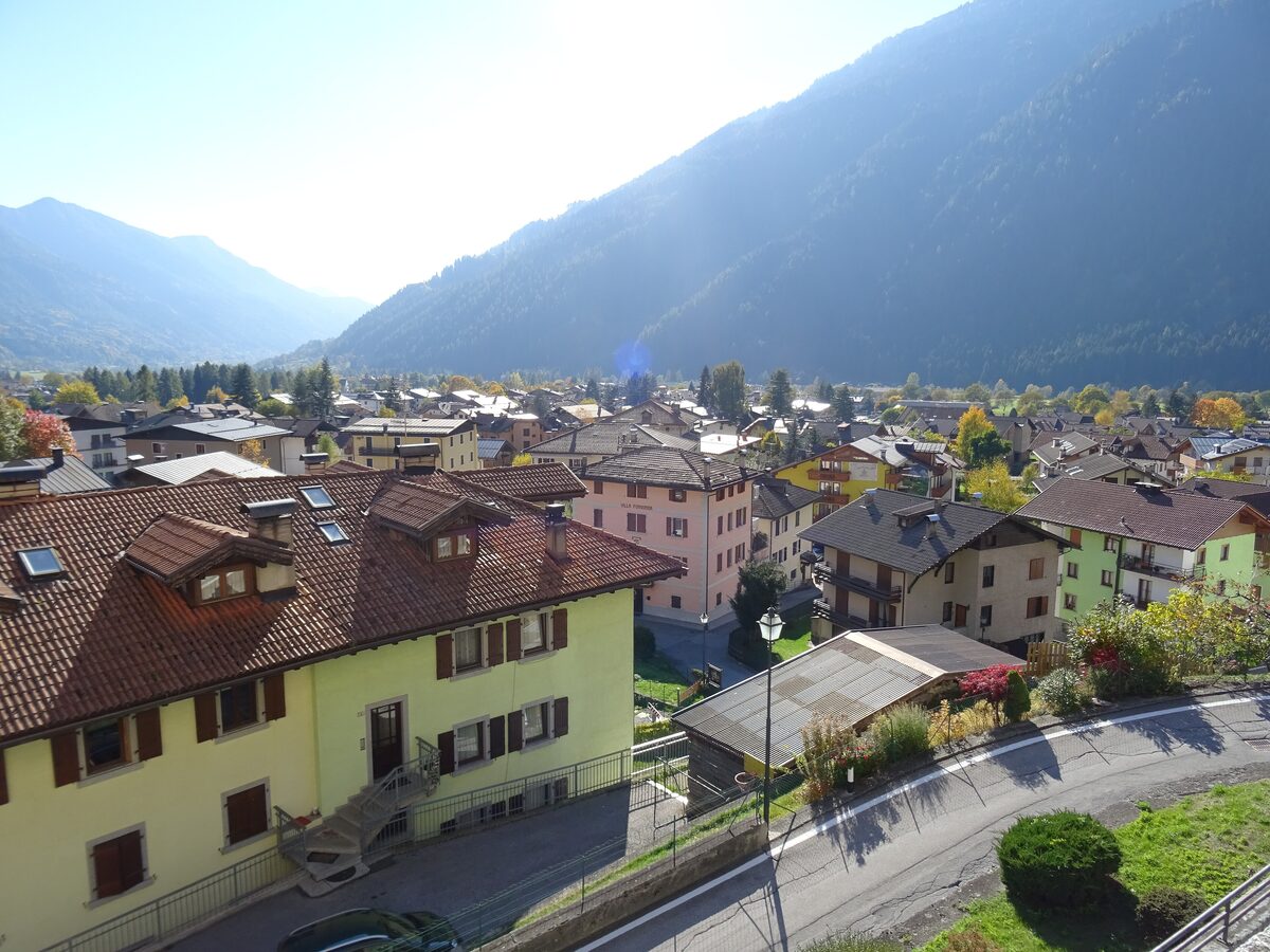 The village of Carisolo in autumn, with rooftops, a road and the wooded valley slope behind