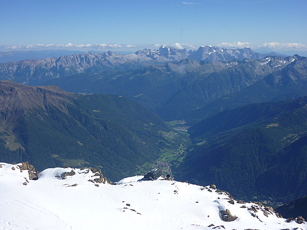 A high mountain view over a green valley and a snowy ridge in the foreground