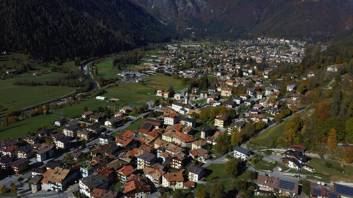 Aerial view of Pinzolo, a compact town of red roofs in the Val Rendena, with forested slopes behind (an autumn shot, no snow)
