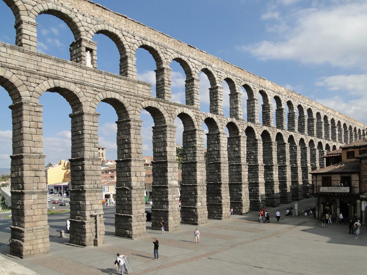The granite arches of the Roman aqueduct rising over the square, with people walking below