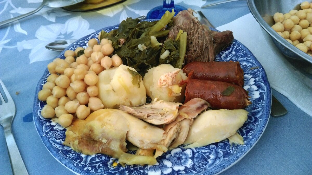 A plate of cocido with chickpeas, cabbage, potatoes, chorizo and chicken on blue-and-white china