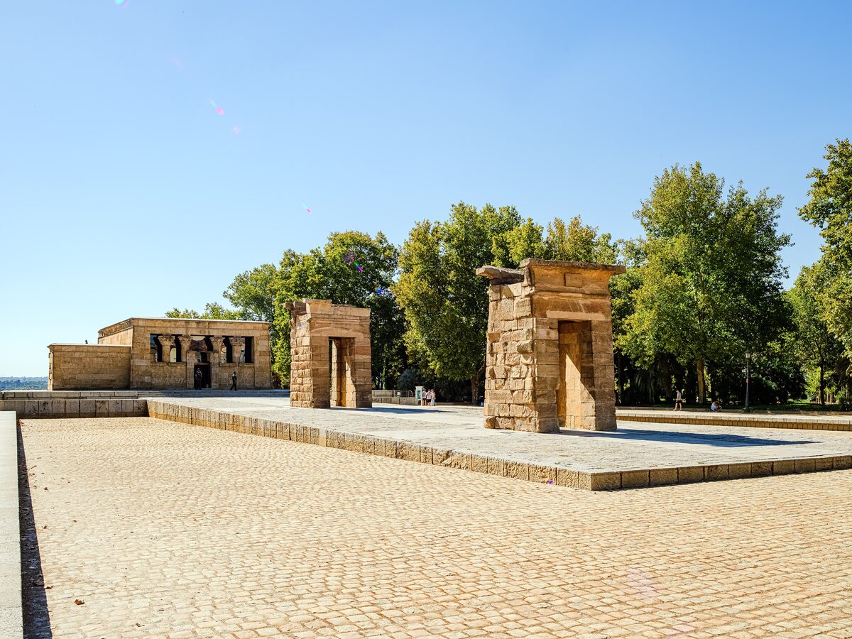 The stone gateways of the Templo de Debod on a paved square, with trees and the pool in front